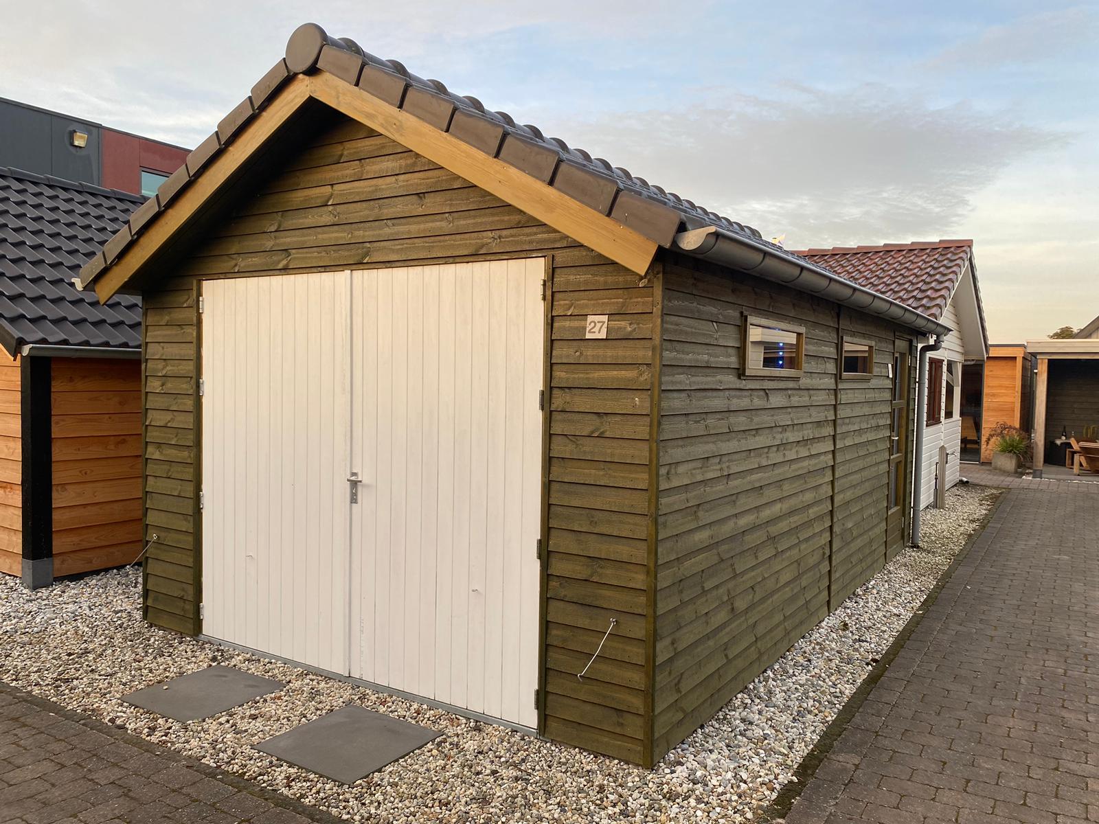 Groen gebeitste houten garage met witte deuren en ramen aan de zijkant